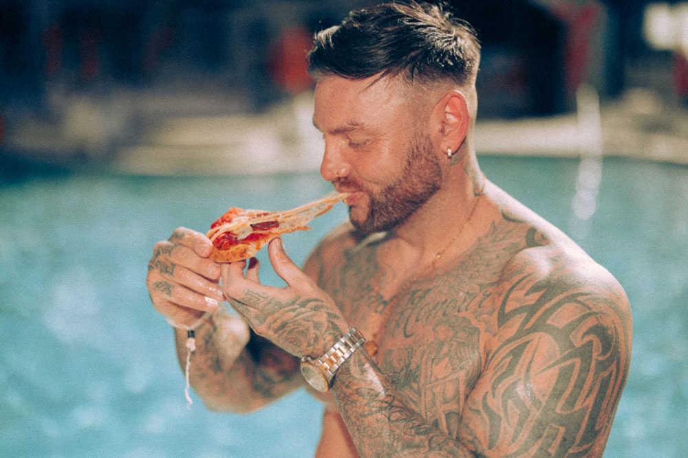 Tattooed man enjoying pizza by the pool at Marina Resort Benidorm