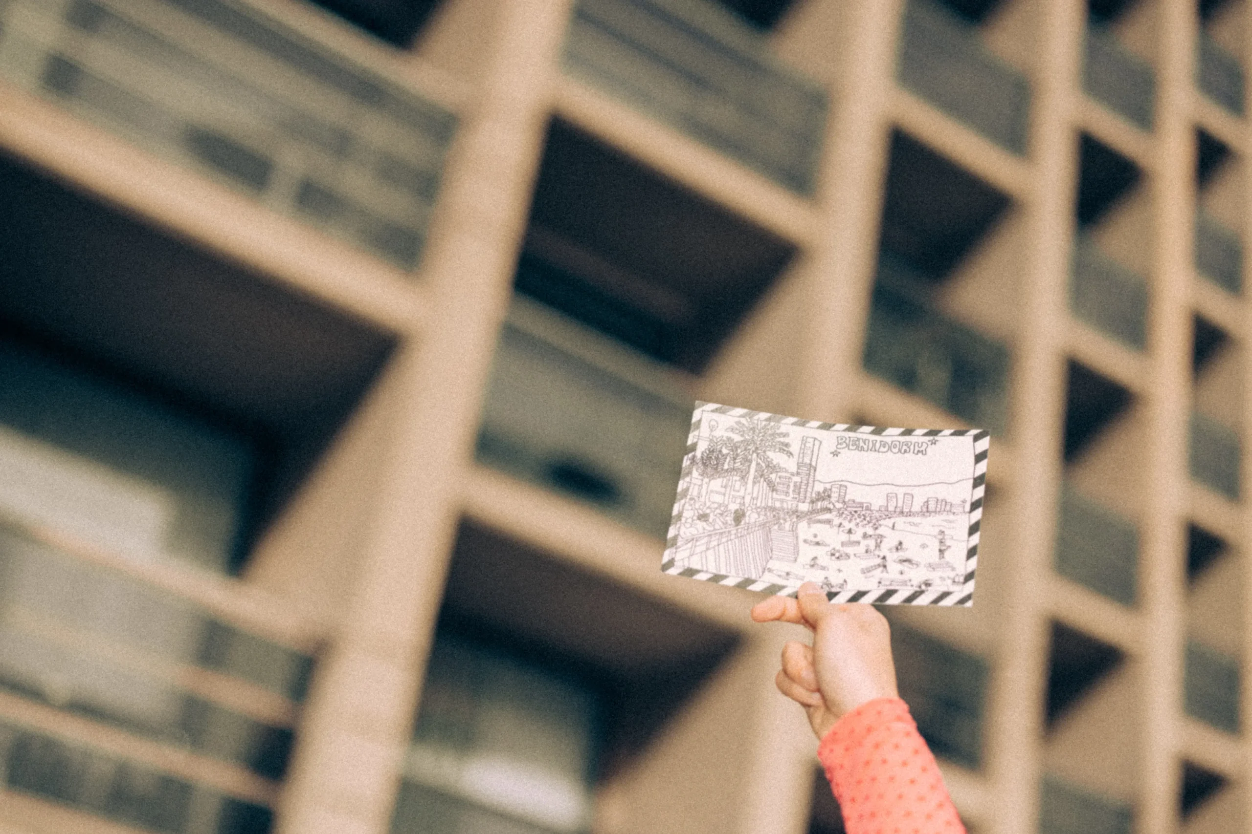 Person holding a Benidorm postcard with a modern building in the background, capturing vacation memories.