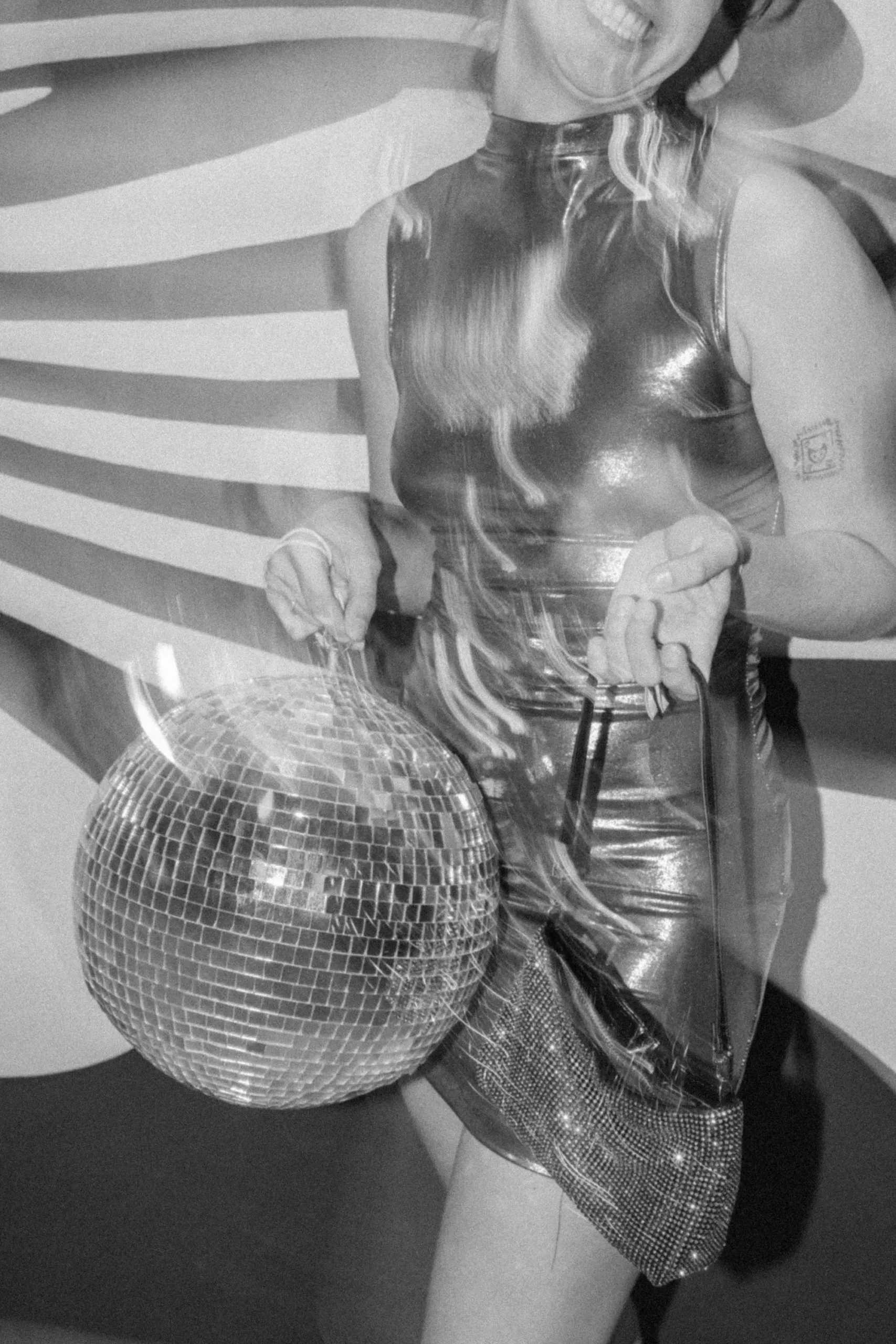 Person in shiny dress holding a disco ball, creating a retro party vibe in black and white style