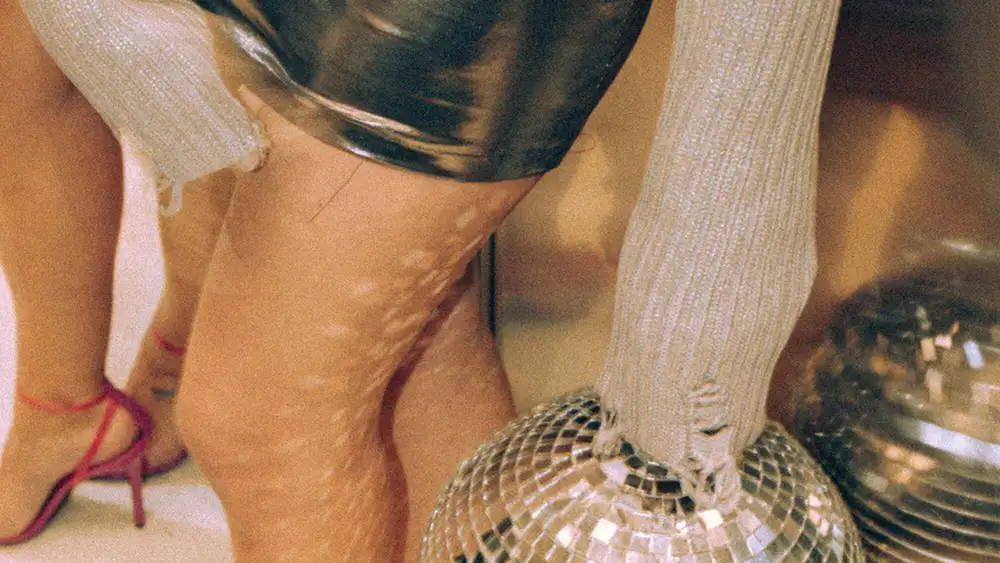 Close-up of a disco ball reflecting light on legs in a party setting with shiny fashion and red heels