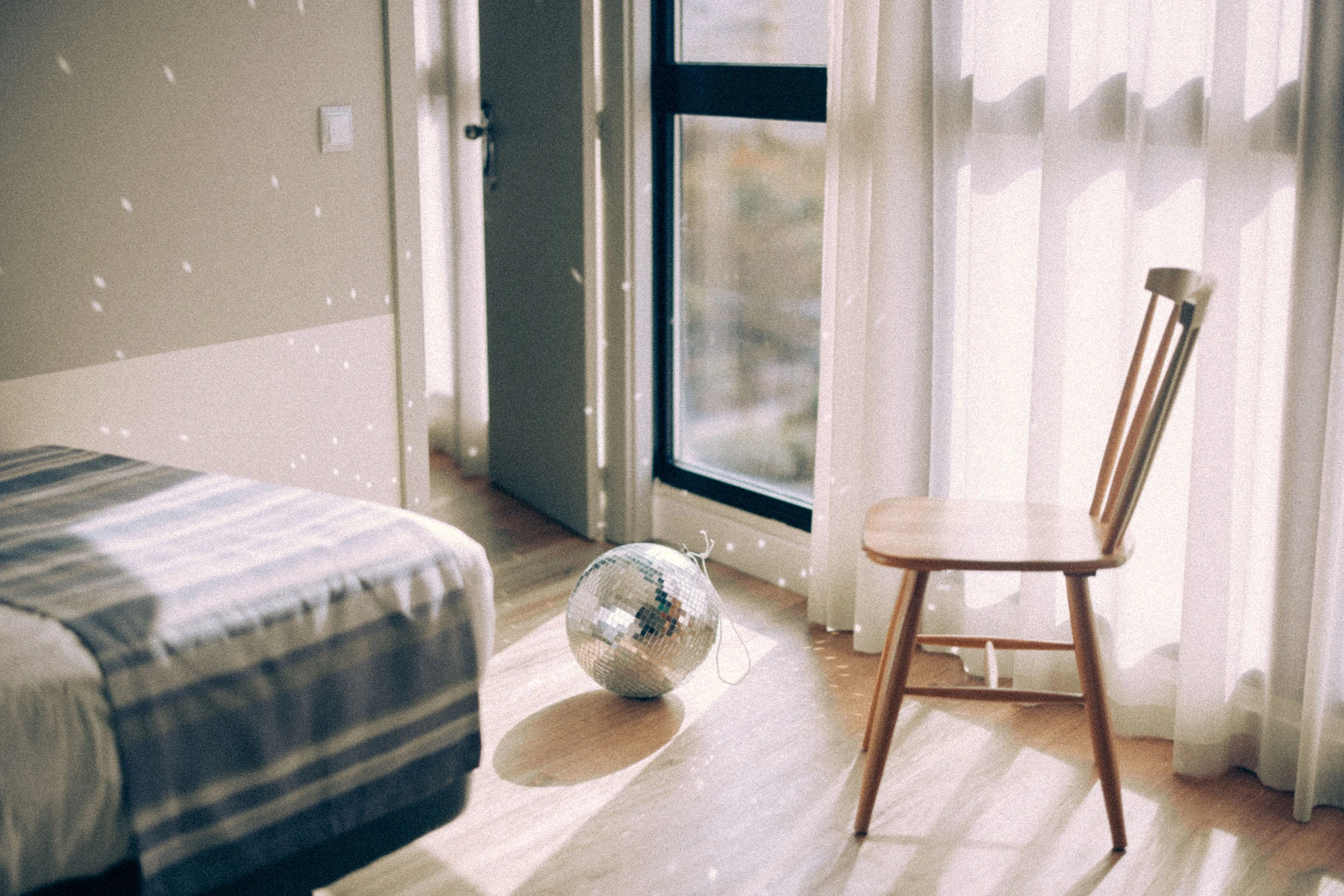 Bright room with sunlight, a wooden chair, and a disco ball reflecting light on the floor.